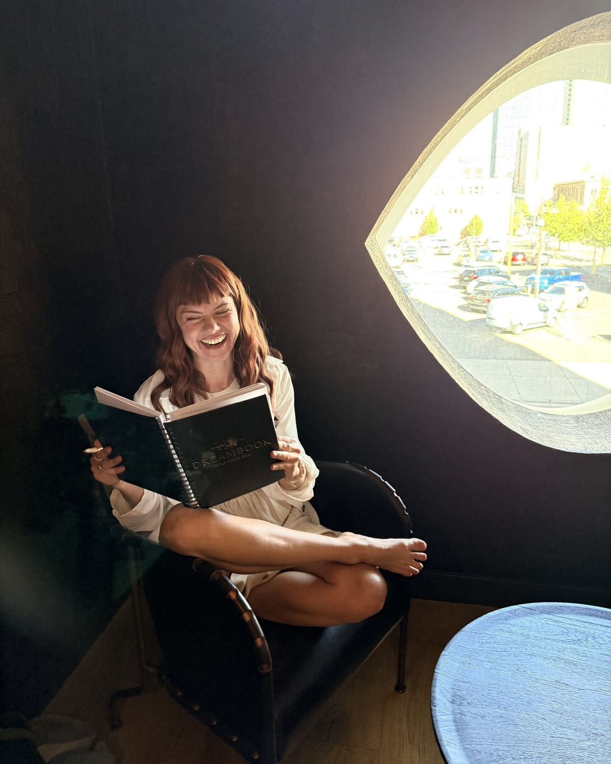 A woman laughing as she reads her Classic Black 2027 Dreambook + Planner