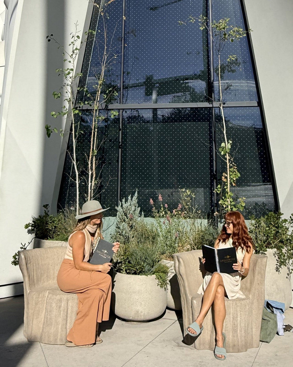 Two women reading their Dreambooks outside a tall arched building