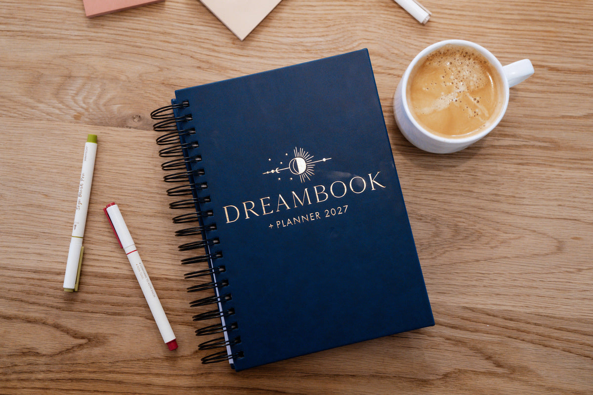 The Nightfall 2027 Dreambook + Planner beside a cup of coffee and pens