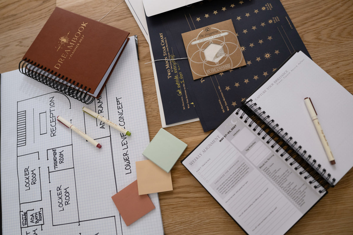 The Saddle 2027 Dreambook, an open Weekly Alignment spread, and a Two Moon Star Chart on a table