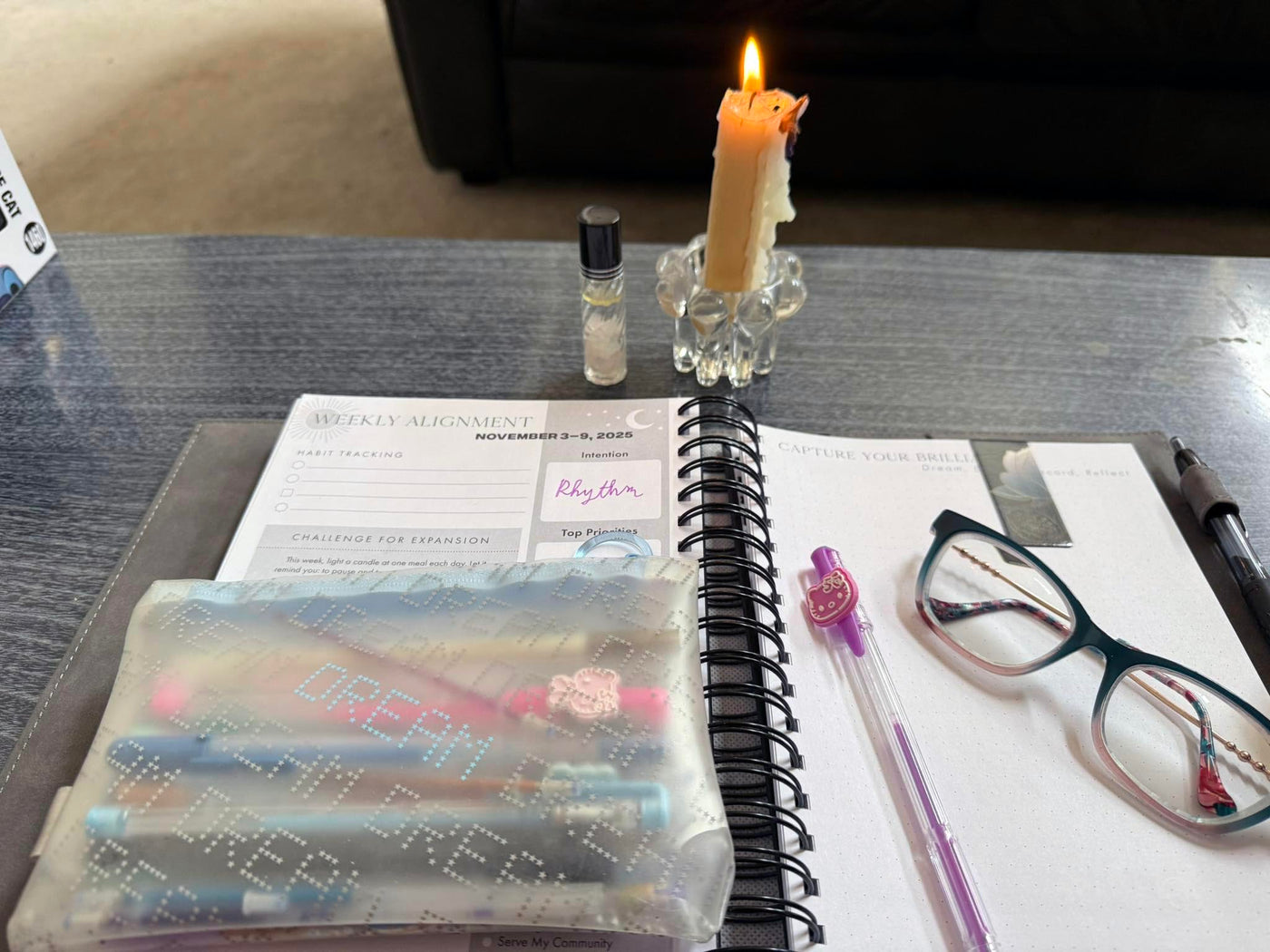 A Dreambook + Planner in Classic Black open on a desk beside glasses and a candle