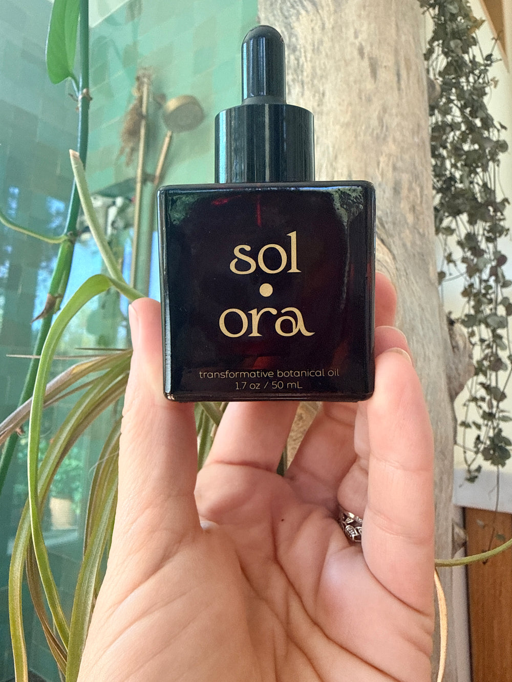 A hand holding up the amber Sol Ora bottle