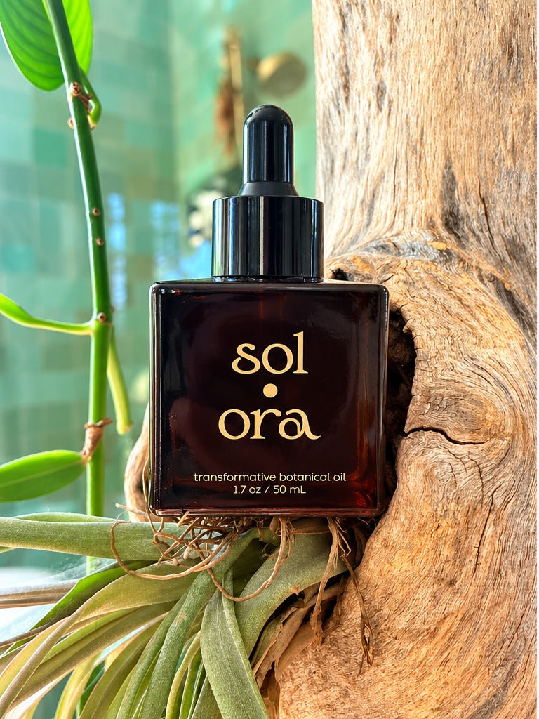 The Sol Ora bottle resting on driftwood among green leaves
