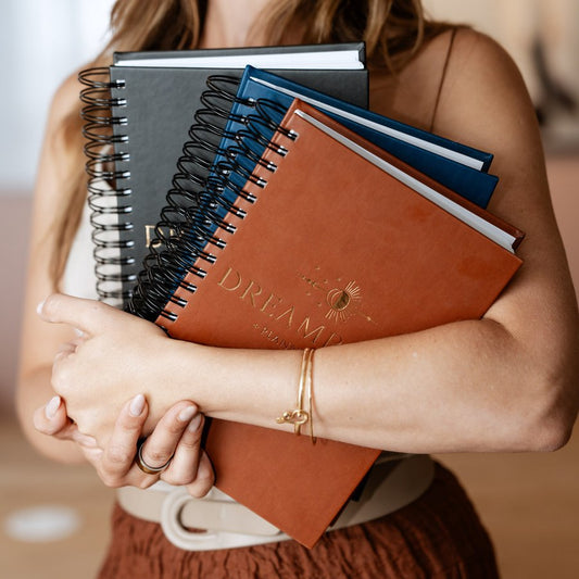 A woman holding the 2027 Dreambook + Planner in Classic Black, Nightfall, and Saddle
