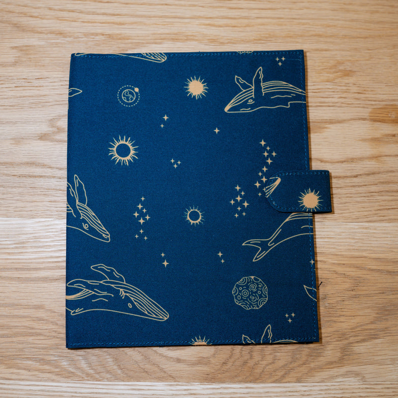 A navy cover printed with gold whales, stars, and planets
