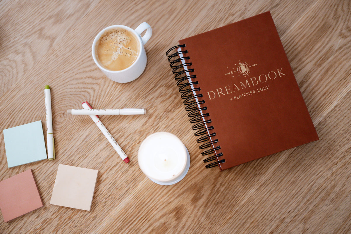 The Saddle 2027 Dreambook + Planner on a table with coffee, pens, and a candle