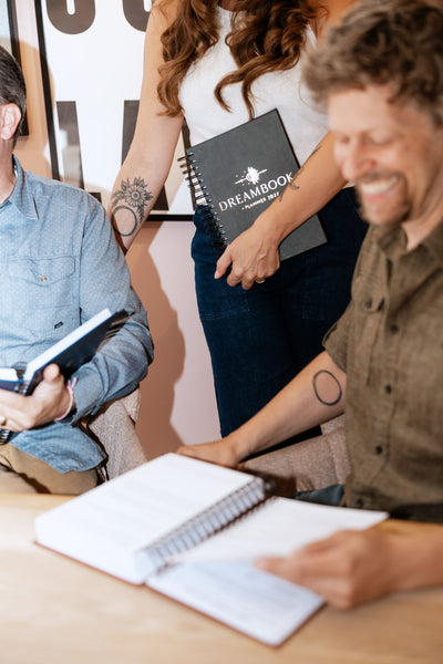 Friends laughing over their Dreambooks, one holding the Classic Black 2027 edition